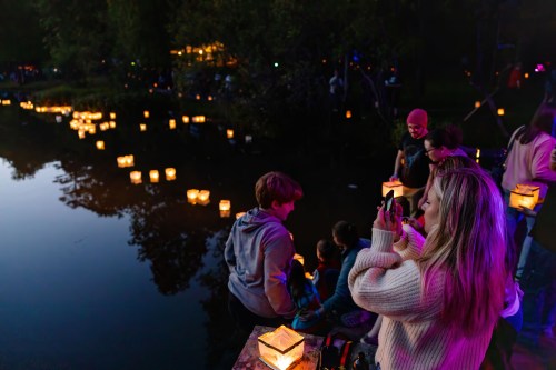 A group of people by a pond at night, enjoying glowing lanterns floating on the water.