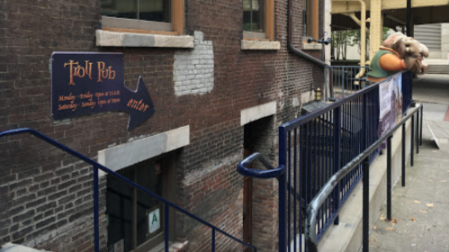 A brick building with a sign for "Troll Pub" and a whimsical troll statue near the entrance.