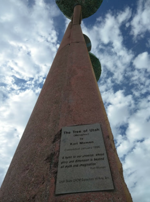 A tall sculpture titled "The Tree of Utah" by Karl Momen, with a plaque at its base, under a cloudy sky.