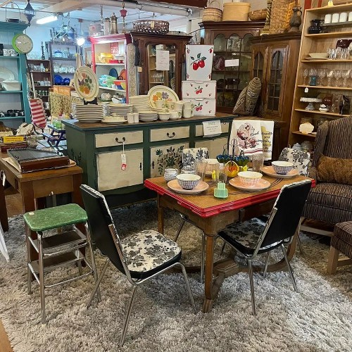 A cozy vintage dining area with a wooden table, patterned chairs, and a green sideboard surrounded by various decor items.