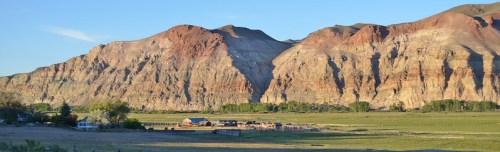A scenic view of colorful mountains rising above a rural landscape with a small farm in the foreground.