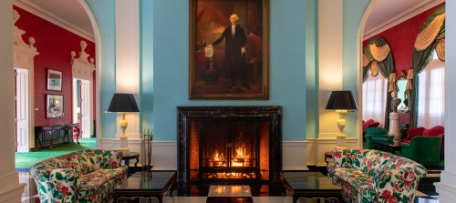 Cozy interior with floral sofas, a fireplace, and a large portrait of a historical figure on the wall.