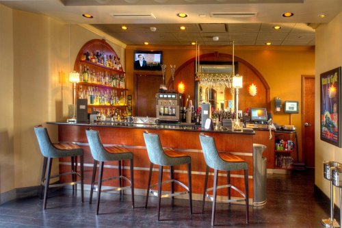 A stylish bar with high stools, a well-stocked shelf of liquor, and warm lighting in a modern setting.