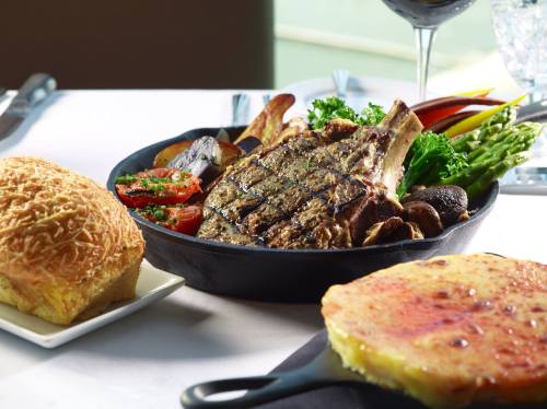 A beautifully plated meal featuring a grilled steak, vegetables, and sides, with a bread roll and dessert on the table.