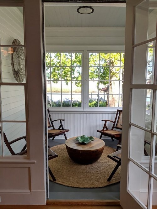 A cozy sunroom with four chairs, a round table, and large windows overlooking greenery.