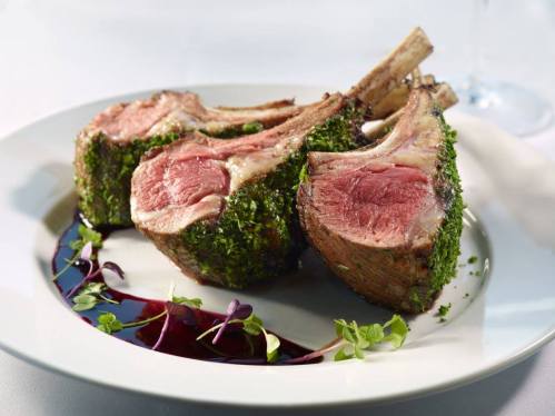 Three perfectly cooked lamb chops with a herb crust, garnished with microgreens and drizzled with a rich sauce.