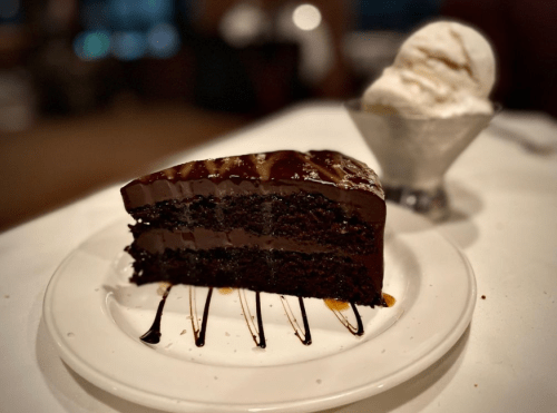 A slice of rich chocolate cake drizzled with sauce, served alongside a scoop of vanilla ice cream.