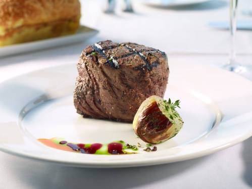 A perfectly grilled steak on a white plate, garnished with a roasted onion and colorful sauces.