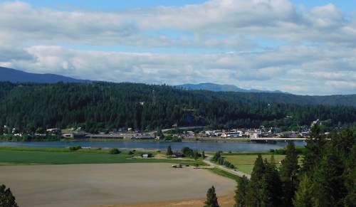 A scenic view of a river town surrounded by lush green hills and fields under a partly cloudy sky.