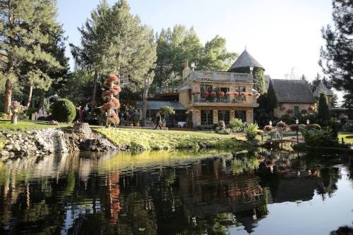 A picturesque house surrounded by trees and a serene pond, featuring lush gardens and decorative sculptures.