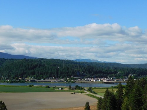 A scenic view of a river surrounded by lush green hills and fields under a blue sky with scattered clouds.