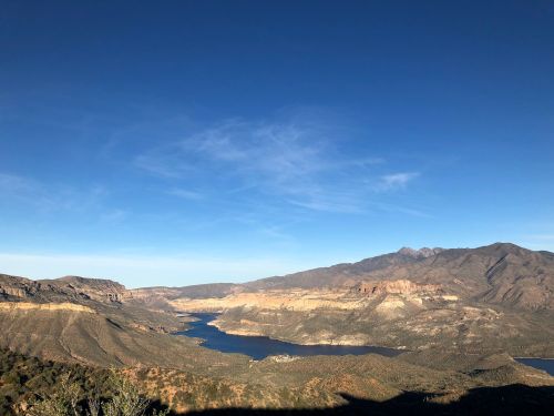 A panoramic view of a serene lake surrounded by mountains under a clear blue sky.