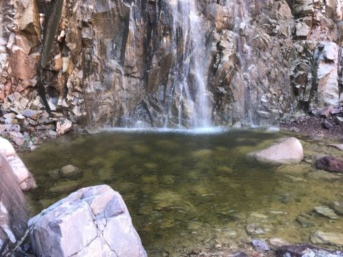 A serene waterfall cascading over rocky cliffs into a clear pool surrounded by stones.