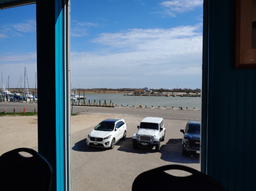 View from a building showing parked cars and a marina with boats on a calm water under a clear blue sky.