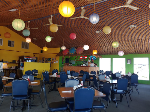 Brightly colored restaurant interior with lanterns, tables, and a bar area, featuring a vibrant yellow and green decor.