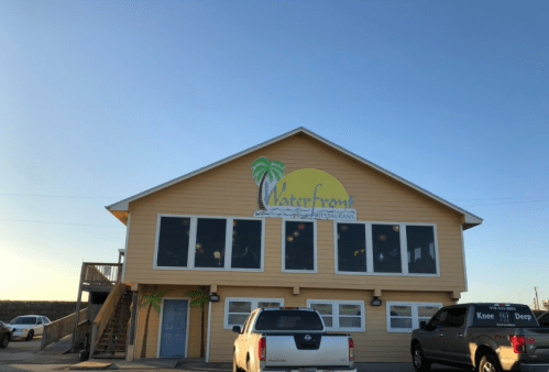 A yellow two-story restaurant with a palm tree logo, located by the waterfront under a clear blue sky.