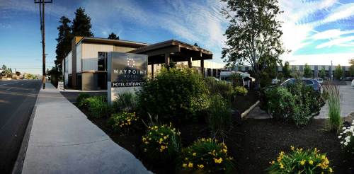 Exterior view of Waypoint Hotel, featuring a sign and landscaped garden, with a clear blue sky in the background.