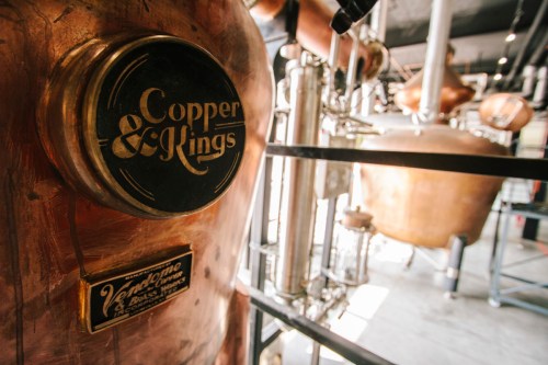 Close-up of a copper distillery still labeled "Copper & Kings," showcasing industrial brewing equipment.