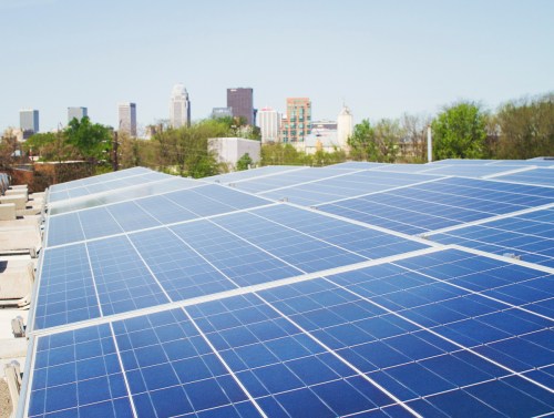 Solar panels on a rooftop with a city skyline in the background under a clear blue sky.