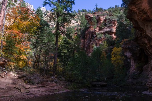 A serene landscape featuring colorful autumn trees, rocky cliffs, and a calm water body surrounded by greenery.