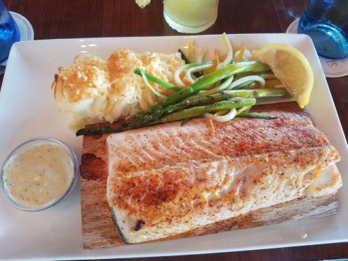 A plate featuring grilled salmon, asparagus, green beans, and a side of creamy baked potato, garnished with lemon.