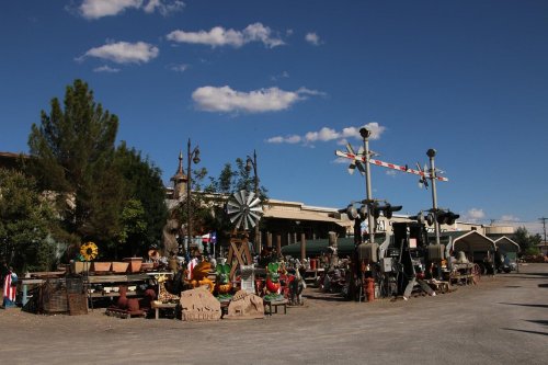 A rustic outdoor market with various decorations, plants, and vintage items under a clear blue sky.