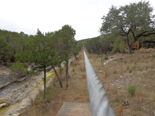A long cable stretches through a wooded area, with trees and rocky terrain on either side.