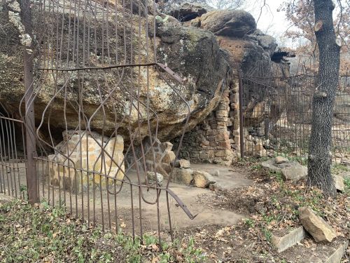 A rocky outcrop with a gated entrance, surrounded by trees and overgrown vegetation.