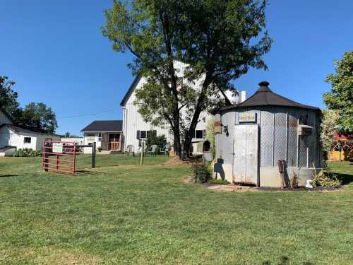 A sunny farm scene featuring a barn, a round water tank, and green grass under a clear blue sky.