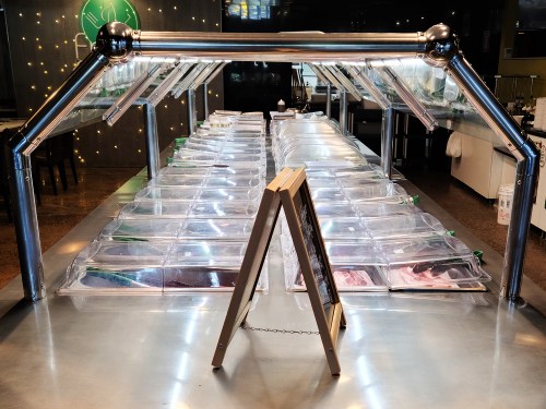 A seafood display with transparent containers under bright lights, showcasing various types of fish and seafood.