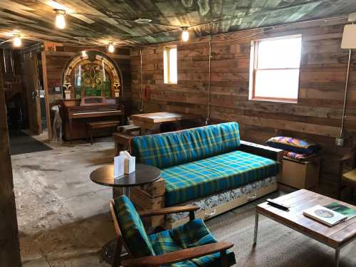 Cozy interior of a rustic room with wooden walls, a colorful couch, tables, and a stained glass window.