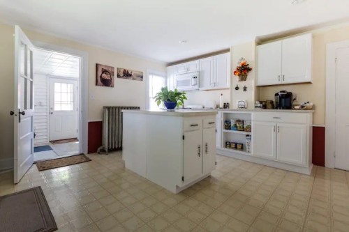 Bright kitchen with white cabinets, an island, and a door leading to an entryway. Plants and decor add warmth.