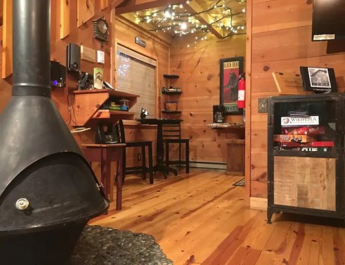 Cozy wooden interior with a black stove, warm lighting, and rustic furniture, creating a welcoming atmosphere.