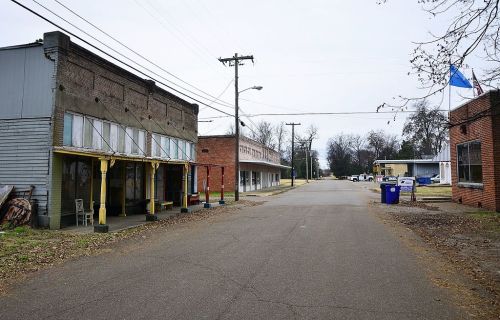 A quiet, empty street lined with old storefronts and utility poles, under a cloudy sky.
