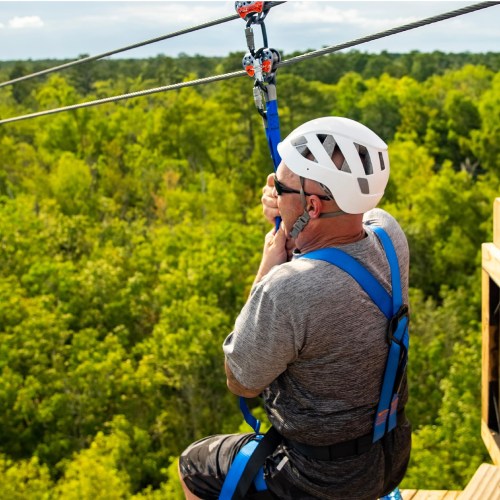 A person in a helmet and harness prepares to zip line over a lush green landscape.