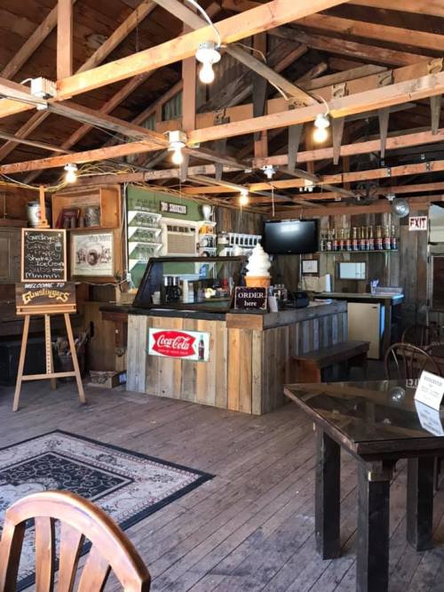 Cozy rustic café interior with wooden beams, a counter, and tables, featuring a Coca-Cola sign and a chalkboard menu.