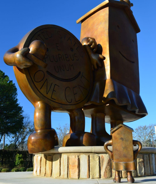 A large bronze sculpture of a coin and a boxy character, both smiling, against a clear blue sky.
