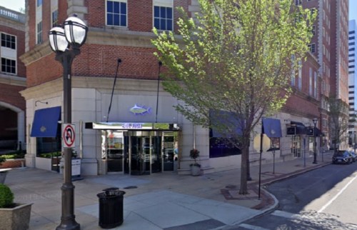 Exterior view of a brick building with large glass doors, trees, and street lamps in an urban setting.