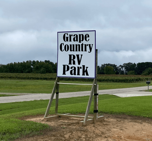 Sign for Grape Country RV Park, featuring bold black text on a white background, set against a grassy landscape.