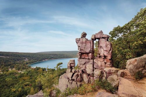 Rock formations overlook a serene lake surrounded by lush greenery under a clear blue sky.