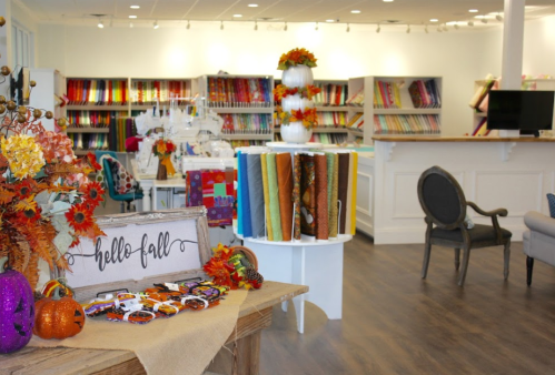 A cozy fabric store decorated for fall, featuring colorful fabrics, pumpkins, and autumn-themed decor.