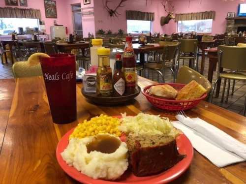 A plate of meatloaf with mashed potatoes, corn, and salad, alongside a drink and bread in a cozy café setting.