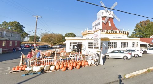 A quaint shop with a windmill sign, featuring pumpkins and gourds outside, set in a rural area.