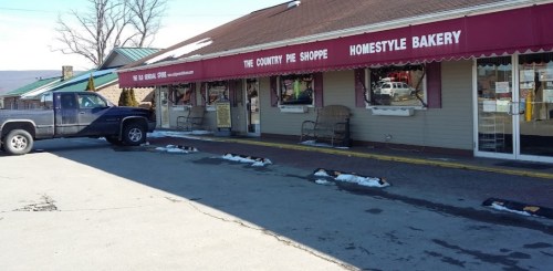 A bakery storefront with a red awning, parked truck, and snow patches on the ground.
