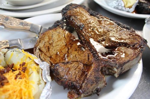 A juicy, grilled steak on a plate, glistening with juices, alongside a baked potato topped with cheese and bacon.