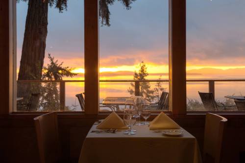 A dining table set for two, with a stunning sunset view over water and trees through large windows.