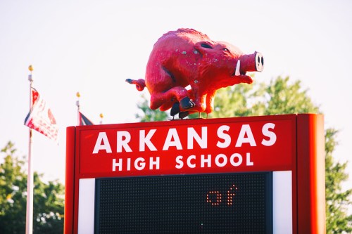 A large red hog statue atop a sign that reads "Arkansas High School," surrounded by trees and flags.