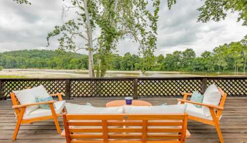 A cozy wooden deck with two chairs and a table, overlooking a serene landscape of trees and water under a cloudy sky.