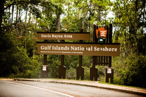 Sign for Gulf Islands National Seashore, Davis Bayou Area, surrounded by trees and greenery.