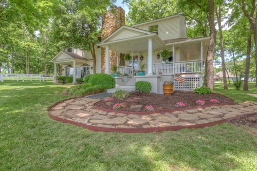 A charming house with a stone pathway, surrounded by lush greenery and colorful flowers in a serene outdoor setting.